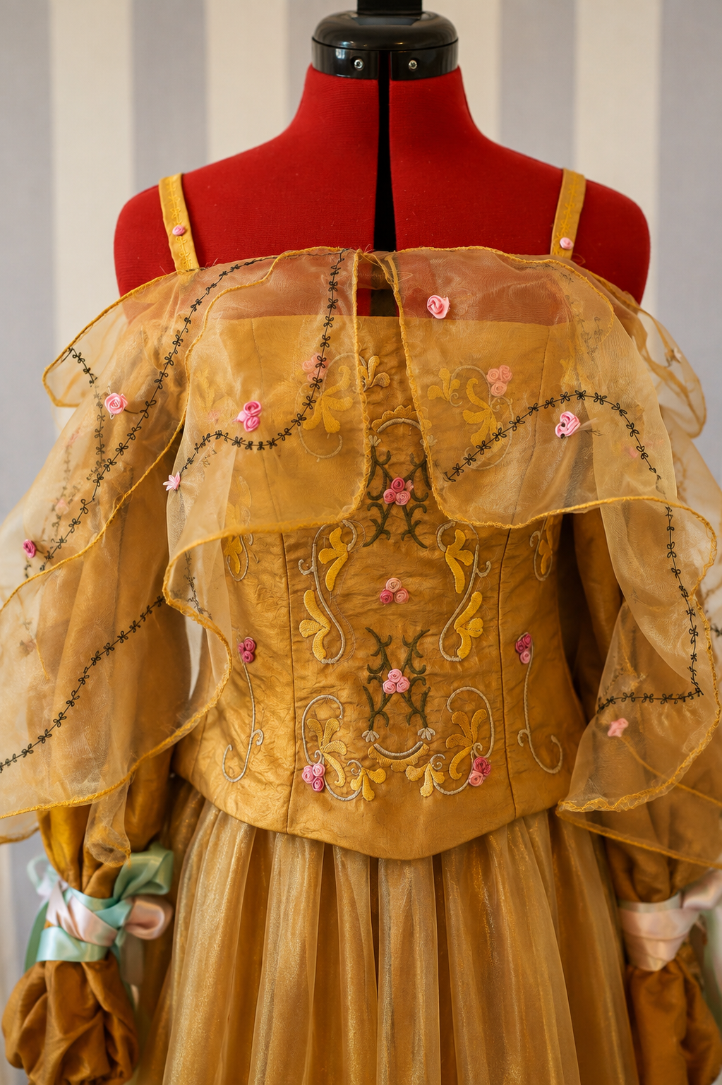 Close-up of golden embroidered corset with pink floral details and sheer organza cape on fantasy gown