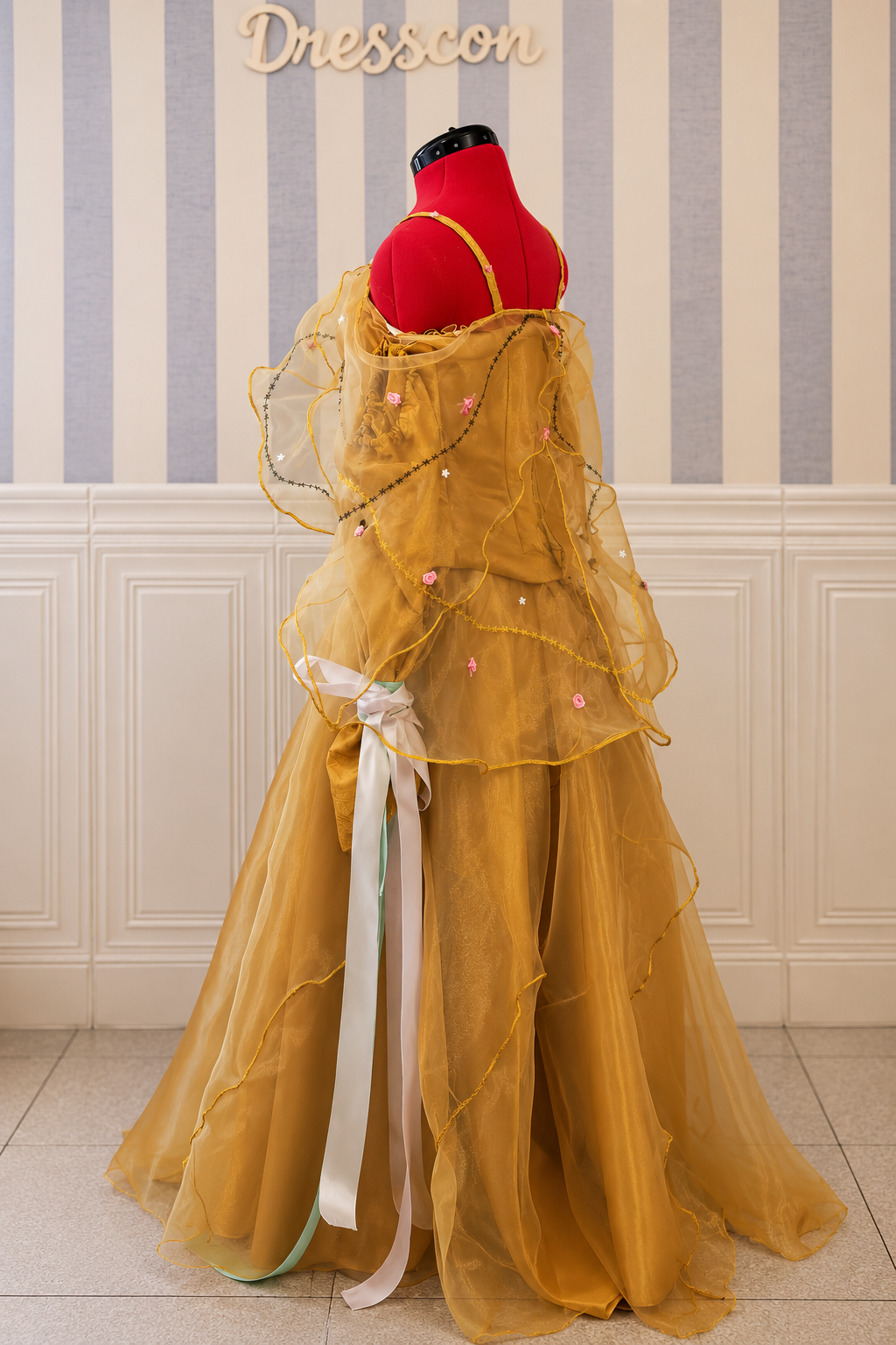 Three-quarter back view of golden fantasy gown with layered organza cape, pastel ribbons and full floor-length skirt