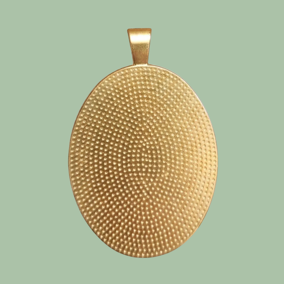 Back view of the Marie Antoinette oval medallion showing the textured gold-toned brass setting on a muted sage green background.